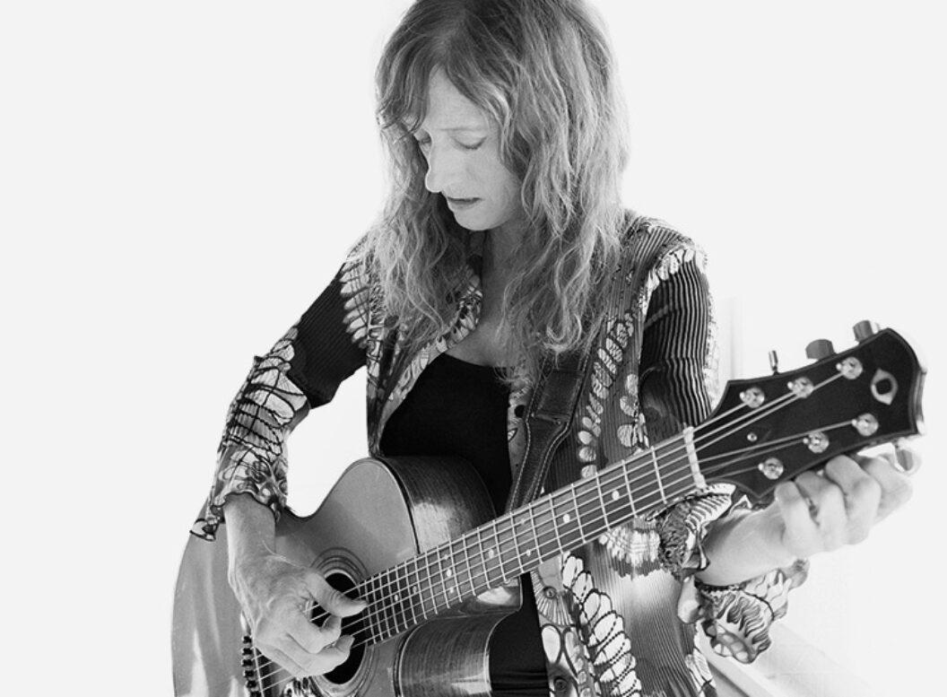 Black and white photograph of Patty Larkin looking down at and tuning an acoustic guitar