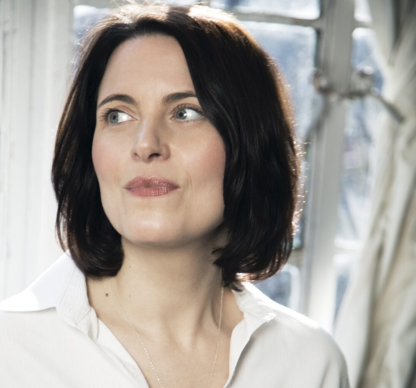 A white woman with a white shirt and shoulder-length brown hair.